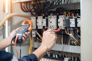 Elektrik mühendisi elektrik kabinesi kontrolündeki voltaj ve elektrik akımını ölçen bir testçi, elektrik sisteminin işleyişini konsept olarak kontrol ediyor .