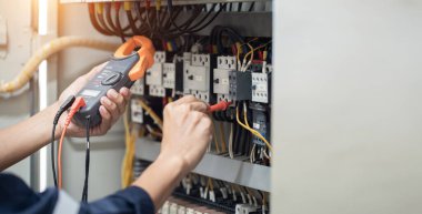 Elektrik mühendisi elektrik kabinesi kontrolündeki voltaj ve elektrik akımını ölçen bir testçi, elektrik sisteminin işleyişini konsept olarak kontrol ediyor .