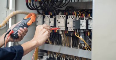 Elektrik mühendisi elektrik kabinesi kontrolündeki voltaj ve elektrik akımını ölçen bir testçi, elektrik sisteminin işleyişini konsept olarak kontrol ediyor .