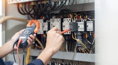 Elektrik mühendisi elektrik kabinesi kontrolündeki voltaj ve elektrik akımını ölçen bir testçi, elektrik sisteminin işleyişini konsept olarak kontrol ediyor .