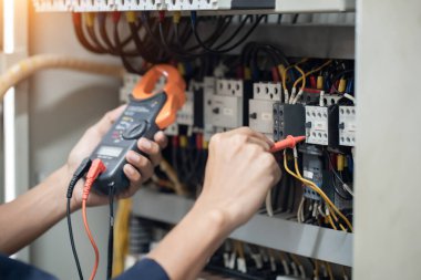 Elektrik mühendisi elektrik kabinesi kontrolündeki voltaj ve elektrik akımını ölçen bir testçi, elektrik sisteminin işleyişini konsept olarak kontrol ediyor .