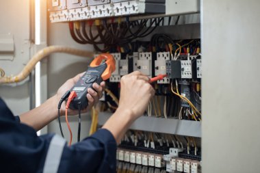 Elektrik mühendisi elektrik kabinesi kontrolündeki voltaj ve elektrik akımını ölçen bir testçi, elektrik sisteminin işleyişini konsept olarak kontrol ediyor .