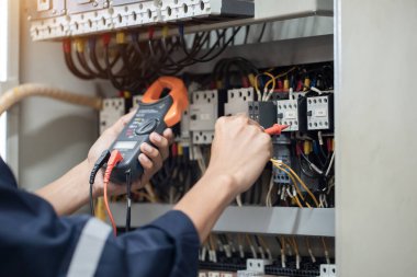 Elektrik mühendisi elektrik kabinesi kontrolündeki voltaj ve elektrik akımını ölçen bir testçi, elektrik sisteminin işleyişini konsept olarak kontrol ediyor .