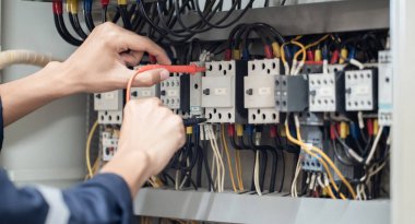 Elektrik mühendisi elektrik kabinesi kontrolündeki voltaj ve elektrik akımını ölçen bir testçi, elektrik sisteminin işleyişini konsept olarak kontrol ediyor .