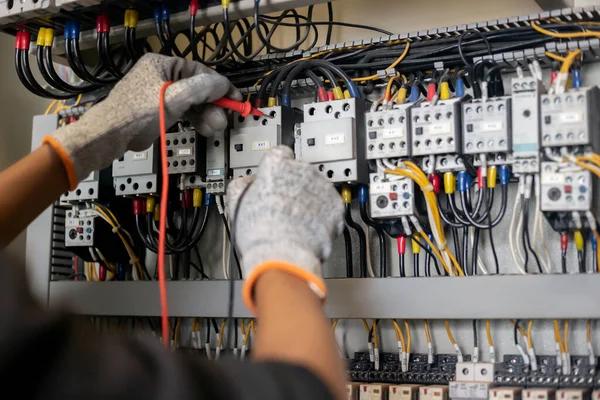 Electrician engineer uses a multimeter to test the electrical installation and power line current in an electrical system control cabinet.