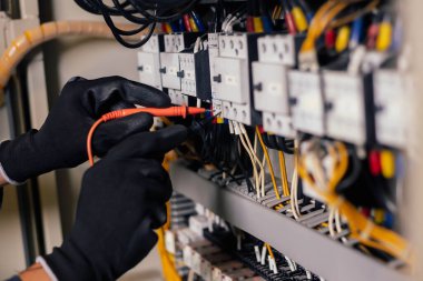Elektrik mühendisi, elektrik kabinesi kontrolündeki voltaj ve elektrik akımını ölçen bir testçi ve röle koruma sistemindeki kabloları kontrol ediyor. Körfez kontrol birimi. Orta gerilim şalteri.