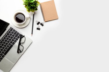 Üst kattaki ofis masasında yatıyordu. Çalışma alanı boş dizüstü bilgisayar, ofis malzemeleri, kalem, yeşil yaprak ve beyaz arka planda kahve fincanı.