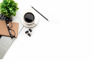 Üst kattaki ofis masasında yatıyordu. Çalışma alanı boş dizüstü bilgisayar, ofis malzemeleri, kalem, yeşil yaprak ve beyaz arka planda kahve fincanı.