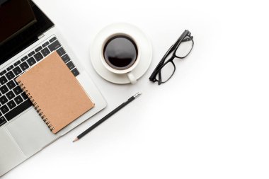 Üst kattaki ofis masasında yatıyordu. Çalışma alanı boş dizüstü bilgisayar, ofis malzemeleri, kalem, yeşil yaprak ve beyaz arka planda kahve fincanı.
