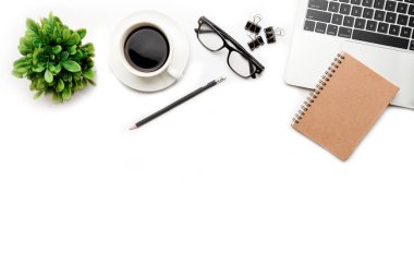 Üst kattaki ofis masasında yatıyordu. Çalışma alanı boş dizüstü bilgisayar, ofis malzemeleri, kalem, yeşil yaprak ve beyaz arka planda kahve fincanı.