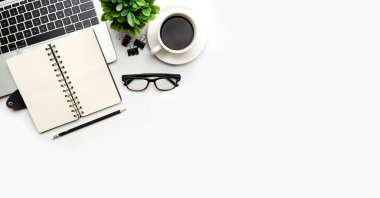 Üst kattaki ofis masasında yatıyordu. Çalışma alanı boş dizüstü bilgisayar, ofis malzemeleri, kalem, yeşil yaprak ve beyaz arka planda kahve fincanı.