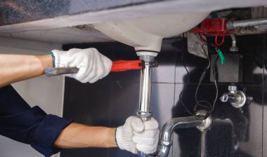 Tesisatçı ayarlanabilir anahtarla beyaz lavabo borusunu tamir ediyor..