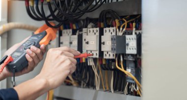 Elektrik mühendisi elektrik kabinesi kontrolündeki voltaj ve elektrik akımını ölçen bir testçi, elektrik sisteminin işleyişini konsept olarak kontrol ediyor .