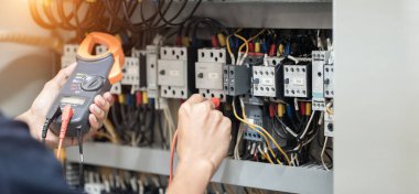 Elektrik mühendisi elektrik kabinesi kontrolündeki voltaj ve elektrik akımını ölçen bir testçi, elektrik sisteminin işleyişini konsept olarak kontrol ediyor .