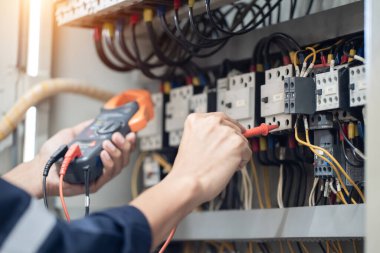 Elektrik mühendisi elektrik kabinesi kontrolündeki voltaj ve elektrik akımını ölçen bir testçi, elektrik sisteminin işleyişini konsept olarak kontrol ediyor .