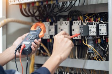 Elektrik mühendisi elektrik kabinesi kontrolündeki voltaj ve elektrik akımını ölçen bir testçi, elektrik sisteminin işleyişini konsept olarak kontrol ediyor .