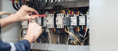 Elektrik mühendisi elektrik kabinesi kontrolündeki voltaj ve elektrik akımını ölçen bir testçi, elektrik sisteminin işleyişini konsept olarak kontrol ediyor .