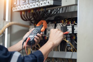 Elektrik mühendisi elektrik kabinesi kontrolündeki voltaj ve elektrik akımını ölçen bir testçi, elektrik sisteminin işleyişini konsept olarak kontrol ediyor .