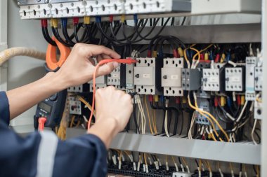 Elektrik mühendisi elektrik kabinesi kontrolündeki voltaj ve elektrik akımını ölçen bir testçi, elektrik sisteminin işleyişini konsept olarak kontrol ediyor .