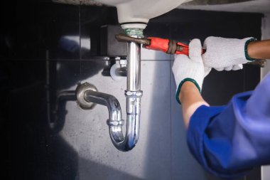 Tesisatçı ayarlanabilir anahtarla beyaz lavabo borusunu tamir ediyor..