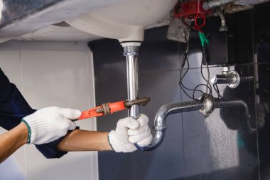 Tesisatçı ayarlanabilir anahtarla beyaz lavabo borusunu tamir ediyor..