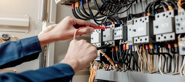 电工工程师用一个万用表来测试电气系统控制柜中的电气装置和电力线路电流 — 图库照片