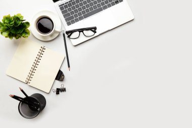 Üst kattaki ofis masasında yatıyordu. Çalışma alanı boş, ofis malzemeleri, kalem, yeşil yaprak ve beyaz arka planda kahve fincanı. .