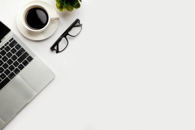 Üst kattaki ofis masasında yatıyordu. Çalışma alanı boş, ofis malzemeleri, kalem, yeşil yaprak ve beyaz arka planda kahve fincanı. .