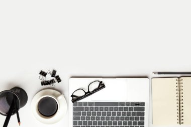 Üst kattaki ofis masasında yatıyordu. Çalışma alanı boş, ofis malzemeleri, kalem, yeşil yaprak ve beyaz arka planda kahve fincanı. .