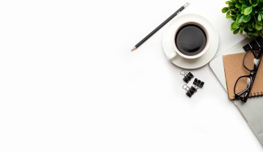 Üst kattaki ofis masasında yatıyordu. Çalışma alanı boş, ofis malzemeleri, kalem, yeşil yaprak ve beyaz arka planda kahve fincanı. .