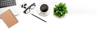 Üst kattaki ofis masasında yatıyordu. Çalışma alanı boş, ofis malzemeleri, kalem, yeşil yaprak ve beyaz arka planda kahve fincanı. .