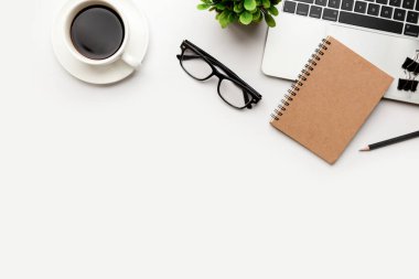 Üst kattaki ofis masasında yatıyordu. Çalışma alanı boş, ofis malzemeleri, kalem, yeşil yaprak ve beyaz arka planda kahve fincanı. .