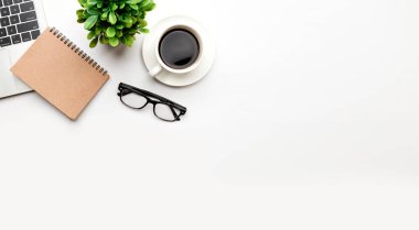 Üst kattaki ofis masasında yatıyordu. Çalışma alanı boş, ofis malzemeleri, kalem, yeşil yaprak ve beyaz arka planda kahve fincanı. .