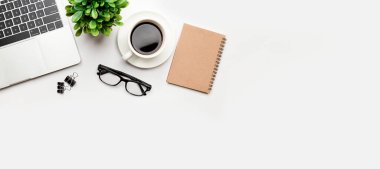 Üst kattaki ofis masasında yatıyordu. Çalışma alanı boş, ofis malzemeleri, kalem, yeşil yaprak ve beyaz arka planda kahve fincanı. .