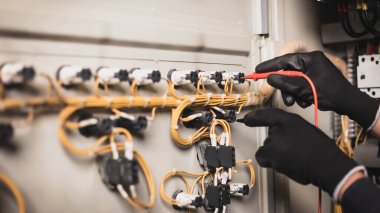 Elektrik mühendisi elektrik kabini kontrolündeki voltaj ve elektrik akımını ölçen bir testçi ve röle koruma sistemindeki kabloları kontrol ediyor. Körfez kontrol birimi. Orta gerilim şalteri.