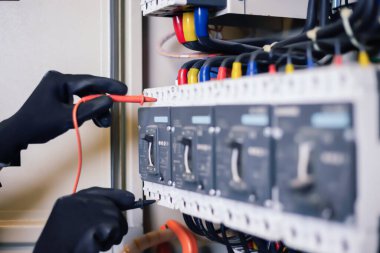 Elektrik mühendisi elektrik kabini kontrolündeki voltaj ve elektrik akımını ölçen bir testçi ve röle koruma sistemindeki kabloları kontrol ediyor. Körfez kontrol birimi. Orta gerilim şalteri.