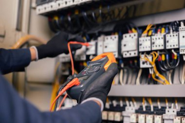 Elektrik mühendisi, elektrik kabinesi kontrolündeki voltaj ve elektrik akımını ölçen bir testçi ve röle koruma sistemindeki kabloları kontrol ediyor. Körfez kontrol birimi. Orta gerilim şalteri.