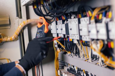 Elektrik mühendisi, elektrik kabinesi kontrolündeki voltaj ve elektrik akımını ölçen bir testçi ve röle koruma sistemindeki kabloları kontrol ediyor. Körfez kontrol birimi. Orta gerilim şalteri.
