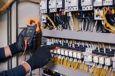 Elektrik mühendisi elektrik kabini kontrolündeki voltaj ve elektrik akımını ölçen bir testçi ve röle koruma sistemindeki kabloları kontrol ediyor. Körfez kontrol birimi. Orta gerilim şalteri.