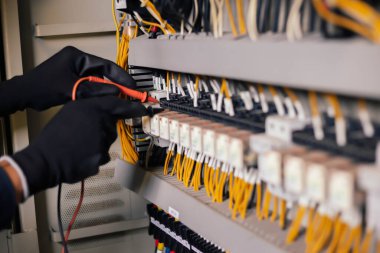 Elektrik mühendisi elektrik kabini kontrolündeki voltaj ve elektrik akımını ölçen bir testçi ve röle koruma sistemindeki kabloları kontrol ediyor. Körfez kontrol birimi. Orta gerilim şalteri.