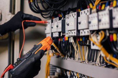 Elektrik mühendisi elektrik kabini kontrolündeki voltaj ve elektrik akımını ölçen bir testçi ve röle koruma sistemindeki kabloları kontrol ediyor. Körfez kontrol birimi. Orta gerilim şalteri.