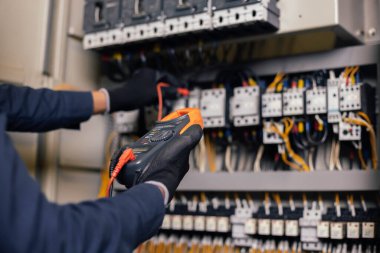 Elektrik mühendisi elektrik kabini kontrolündeki voltaj ve elektrik akımını ölçen bir testçi ve röle koruma sistemindeki kabloları kontrol ediyor. Körfez kontrol birimi. Orta gerilim şalteri.