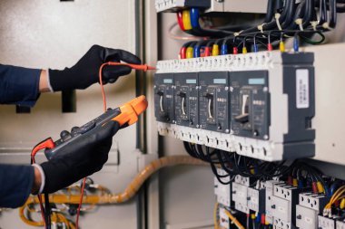 Elektrik mühendisi elektrik kabini kontrolündeki voltaj ve elektrik akımını ölçen bir testçi ve röle koruma sistemindeki kabloları kontrol ediyor. Körfez kontrol birimi. Orta gerilim şalteri.