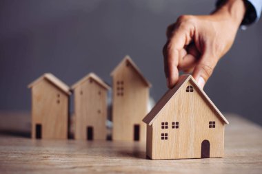 İş adamı ahşap masadan küçük ahşap ev modelini seçiyor, mülk almayı planlıyor. En iyisini seç konsepti.