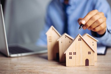 İş adamı ahşap masadan küçük ahşap ev modelini seçiyor, mülk almayı planlıyor. En iyisini seç konsepti.