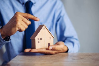 İş adamı ahşap masadan küçük ahşap ev modelini seçiyor, mülk almayı planlıyor. En iyisini seç konsepti.