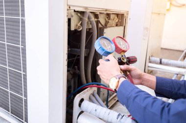 Teknisyen klimayı kontrol ediyor, klimaları doldurmak için ekipmanları ölçüyor..