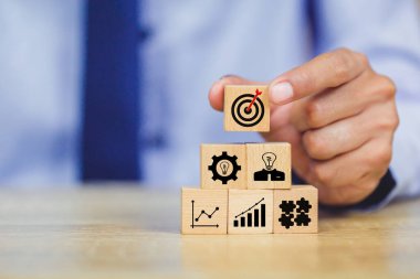 İş başarısı hedefleri kavramı. Yaratıcılık için ahşap küp bloğuna baskı yapan ve iş hedefi hedef kavramı oluşturan el ele tutuşan hedef tahtası, fikirler oluşturmak için engeller, hedef belirleme.