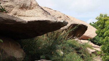 Bitkilerin üzerinde üç büyük kaya ve açık mavi bir gökyüzü.
