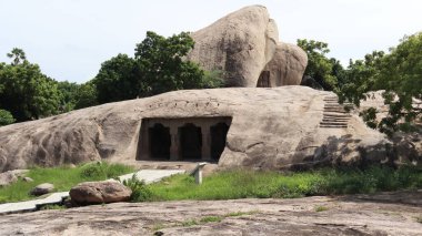 Yere taş oyulmuş bir tapınak. Ve içinde bir sürü heykel var. Doğal arka planda yer alıyor. Bir kenar görünüm.